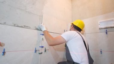 Usta, aletlerin ve yapıştırıcı karışımların yardımıyla banyonun duvarına seramik fayanslar sergiler. İşçi, tamirci, koca, inşaatçı, tiler