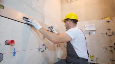 Genç bir inşaatçı duvara seramik fayanslar sergiler. İş sırasında su seviyesini kullanmak. Modern ev yenileme