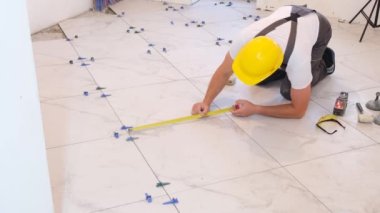 Tulum giyen bir zanaatkar zemine fayanslar döşemiş, evin içini tamir etmiş, inşaat ve apartman onarımı yapmış. Zemine seramik fayanslar yerleştiriliyor - ölçme ve kesme parçaları.