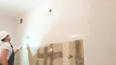 Çalışırken duvarı silindirle boyayan profesyonel bir inşaatçı. Modern tamirat, odanın duvarlarını boyamak.