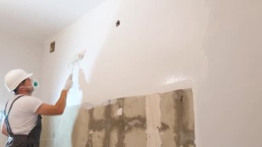 Genç bir adam duvarı beyaza boyuyor. Daire yenileme ustası duvarları boyuyor. Modern ev yenileme