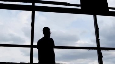 Büyük kırık bir pencerenin önündeki bir adamın silueti. Ukrayna 'daki savaşın sonuçları. Yavaş çekim