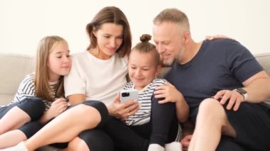 Genç bir aile evdeki kanepede eğleniyor, genç ebeveynler ve çocuklar gülüyor, oynuyor, evde sarılıyor, dinleniyor..