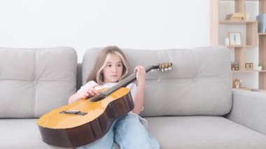 Okul çağındaki bir çocuk evdeki kanepede otururken klasik akustik gitar çalma pratiği yapar. Tembel çocuk, müzik aleti pratiği, ev kavramında karantina boş zamanı