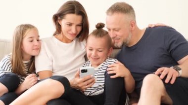Çocuklu genç bir aile kanepede dinleniyor, akıllı telefon kullanıyorlar. İnternete bağımlılık. 4k video