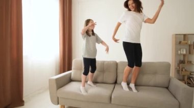 Mutlu anne ve kız kanepede birlikte zıplıyorlar evde tatlı bir kızla eğleniyorlar, genç anne ve çocuk birlikte gülerek vakit geçirmeye bayılıyorlar..