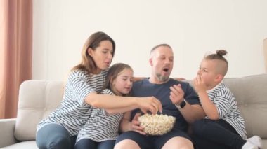 Güzel, çekici, pozitif, neşeli bir ailenin televizyon seyredip patlamış mısır yiyen portresi. Aile boş vakitlerin tadını çıkarıyor. Yüksek kalite 4k video