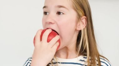 Okul çağındaki bir kız büyük kırmızı bir elma yiyor. Lezzetli sulu meyveler. Çocuklarda sağlıklı dişler. C vitamini