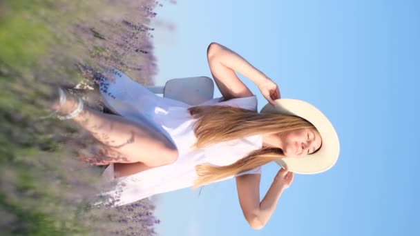 垂直录像 一位戴着白帽的金发姑娘坐在薰衣草花丛中 享受着阳光 薰衣草场的白色照片 — 图库视频影像