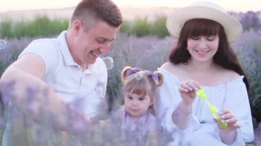 Genç bir adam yazın ailesiyle birlikte dışarıda sabun köpüğü üflüyor. Lavanta tarlasında piknik yapan bir aile. Yüksek kalite 4k video