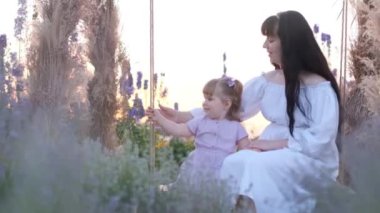 Genç bir anne ve kız salıncakta sallanıyor. Açık hava eğlencesi. Mutlu anne.