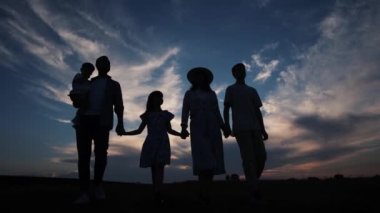Baba, anne ve çocuklar gün batımında parkta yürüyorlar. Gün batımında çocuklarıyla el ele tutuşan ebeveynlerin silueti. Mutlu aile parkta eğleniyor. Aile silueti. Mutlu aile kavramı.
