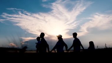 Aile silueti. Baba, anne, kız ve oğul. Sırtlarını kameraya dayayıp gün batımında ufka bakıyorlar. 4k video
