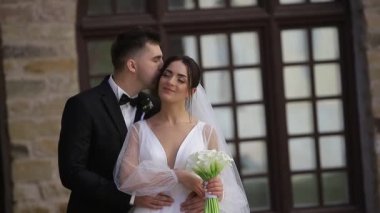 Avrupalı çift düğün günlerinde büyük bir ahşap pencerenin arka planına nazikçe öpüşüyor, mutlu gelin ve damat.