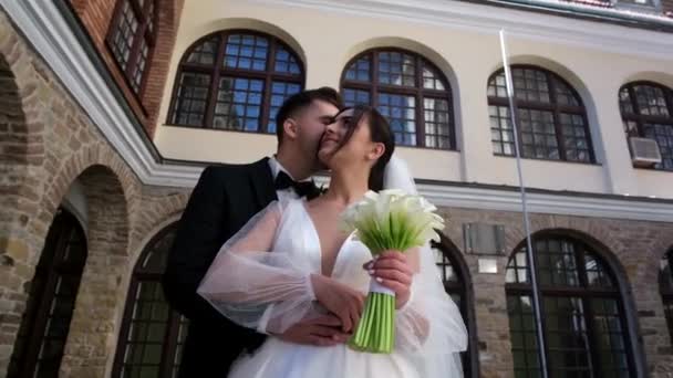 古代ヨーロッパの建築 花嫁と新郎の背景に花の花束と結婚式のドレス交換リングの美しい若いカップル — ストック動画