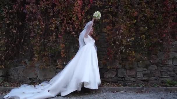 新娘穿着华丽的婚纱 背景是黄色的秋天树叶筑成的墙 欧洲风格的婚礼 幸福的新娘手里拿着一束鲜花 — 图库视频影像