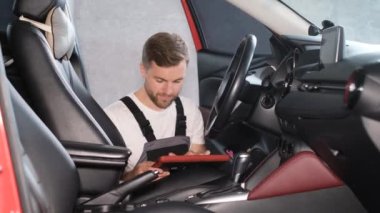 Amerikan görünümlü genç bir araba tamircisi bir tablet kullanarak arabanın teknik durumunu kontrol eder. Yeni bir arabada GPS navigatörü kuruluyor.