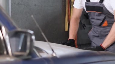 Araba tamir atölyesi. Adamın biri arabanın kaputundan tozu silmiş..