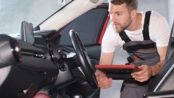 一位年轻的美国汽车修理工用平板电脑检查汽车的技术状况 在新车上安装Gps导航器 — 图库视频影像