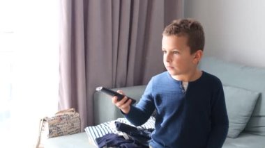 Kanepede oturan küçük bir çocuk televizyonun uzaktan kumandasını elinde tutuyor ve ilginç bir film izliyor. Çocuk televizyon izliyor..