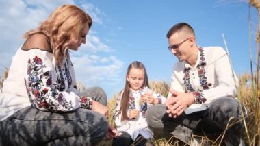 Nakışlı gömleklerle bir Ukraynalı aile, mavi gökyüzüne karşı buğday tarlasının ortasında oturuyor. Mutlu karı koca, birbirlerinin gözlerinin içine bakıyor..