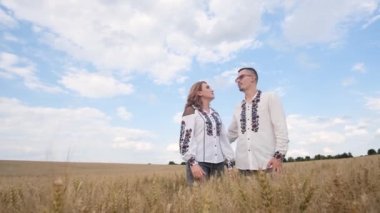 İşlemeli elbiseli Ukraynalı güzel bir çift mavi gökyüzünün arka planında bir şarkı söylüyor. Buğday tarlasında müzik videosu kaydediliyor..