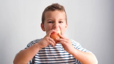 Kırmızı elma yiyen ve kameraya bakan bir çocuğun portresi. Sağlıklı bir çocuk atıştırma sırasında taze meyve yer, sağlıklı bir diyet..