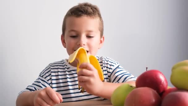 Menino Bonito Com Uma Banana Mão Está Sentado Mesa Cozinha — Vídeo de Stock