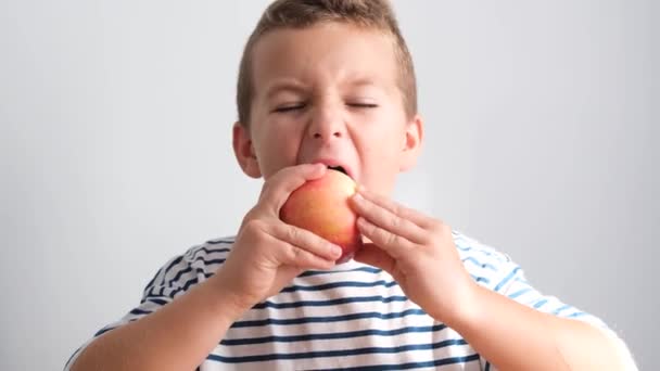 赤ちゃんの男の子はジューシーなリンゴをかむ 朝食に大きな赤いリンゴを食べる子供の顔 4Kビデオ — ストック動画