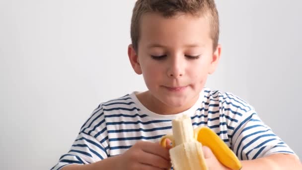 可愛い男の子が白い背景においしい熟したバナナを食べます おいしいトロピカルフルーツ 健康食品 — ストック動画