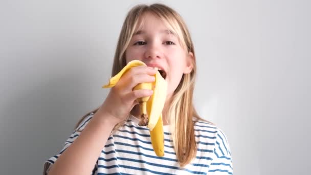 朝食用の果物 金髪の女の子が熟したバナナを食べる 子供たちは学校の前の家庭で台所で朝食をとる おいしい果物 — ストック動画