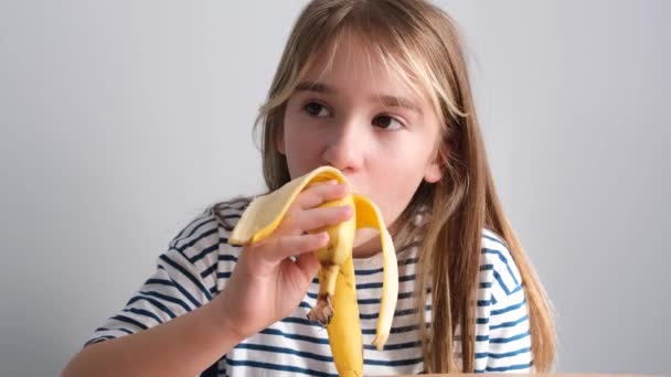 愛らしい小さな学校時代の女の子熟したバナナ 白の背景を食べる おいしいトロピカルフルーツ — ストック動画