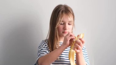 Küçük aç bir kız beyaz arka planda olgun sarı bir muz yiyor. Kız muzu ısırıyor. 4k video