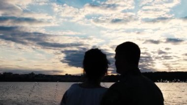 Birbirlerine aşık bir çiftin yakın çekim silueti. Gün batımında göl kenarında öpüşüyorlar. Mutlu bir aile.