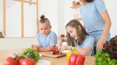 Gülümseyen anne, kız ve oğul modern mutfakta yavaş çekimde eğleniyorlar. Neşeli çocuklar ve anneler mutfakta yemek hazırlıyorlar. Mutlu aile evde birlikte eğleniyor..