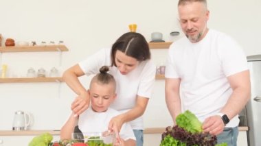 Avrupalı evli bir çift küçük çocuklara mutfakta yemek yapmayı öğretiyor. Bütün aile ev yapımı vejetaryen salatası, modern mutfak, sağlıklı yiyecekler hazırlıyor.