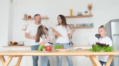 Genç aktif aile evde yemek pişiriyor, kaygısız koca, eş ve çocuklar eğleniyor, dans edip sarılıyorlar.