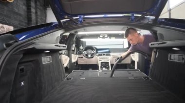 Genç bir adam bir arabanın bagajını süpürüyor. Profesyonel araba temizliği.