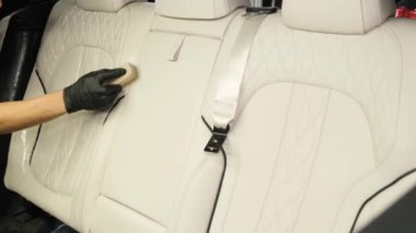 Ahşap bir fırçayla deri araba koltuklarını temizlemek. Araba servisinde profesyonel araba temizliği. Açık renkli araba koltuğu
