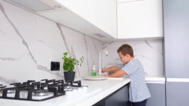 Küçük tatlı okul çocuğu modern mutfakta meyve yıkıyor. Sağlıklı bebek maması.