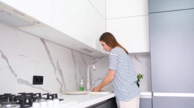 Avrupalı görünümlü genç bir kadın modern beyaz bir mutfakta lavaboda meyve yıkıyor. Sağlıklı yemek yemek.