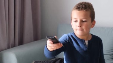 Gri bir kanepede oturan ve elinde uzaktan kumanda tutan sevimli bir çocuğun portresi. Küçük bir öğrenci TV 'de kanal değiştiriyor.