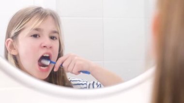 Genç bir kız banyo aynasının önünde dişlerini dikkatlice fırçalar. Çocukların diş sağlığı.