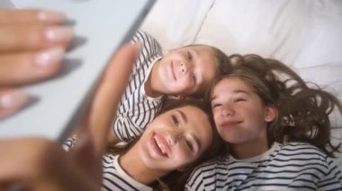 Anne, küçük kız ve oğlu yerde yatarken selfie çekiyorlar. Evde mutlu aile zamanları.