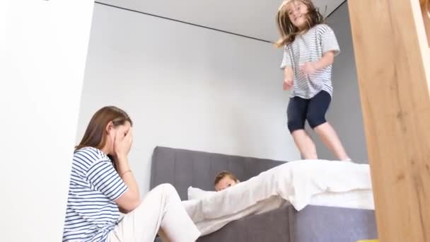いたずらな子供と疲れた母親 安静な男の子と女の子は寝室のベッドの上でジャンプします 週末は家で — ストック動画
