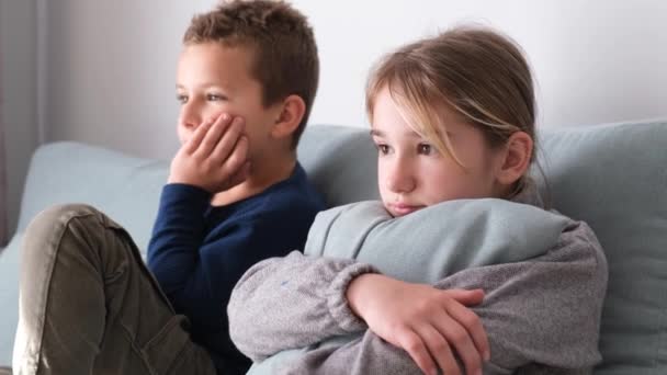 女の子と男の子がリビングでテレビを見ていて 灰色のソファに座っている 子供たちは週末家にいる 子供の漫画を見る — ストック動画