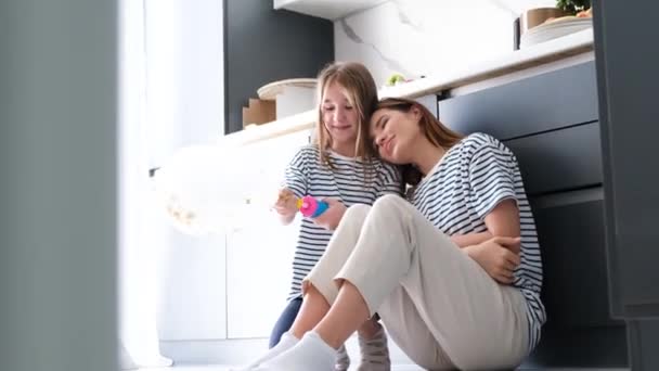 一个年轻的女人坐在现代化厨房的地板上 一边看着电话 年轻的母亲和女儿 一个带着气球的孩子 — 图库视频影像