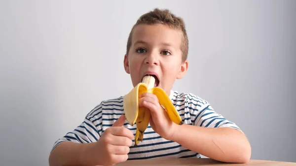Przystojny Chłopiec Koszuli Nocnej Zjada Żółtego Banana Białym Odosobnionym Tle — Zdjęcie stockowe