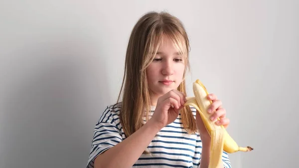 空腹の少女は白い背景に熟した黄色のバナナを食べる 女の子はバナナを噛んだ 4Kビデオ — ストック写真