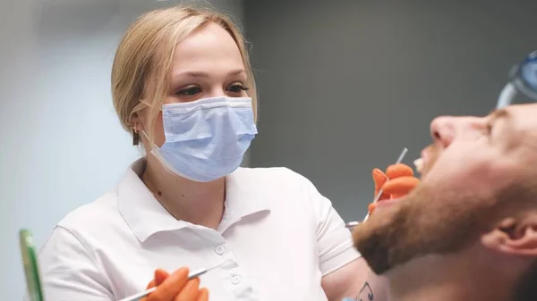 Young blonde doctor treats young mans teeth. The patient sits in the dentists office with his mouth open. Modern painless dental treatment